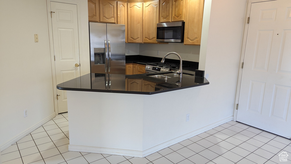 Kitchen with dark countertops, light tile patterned floors, appliances with stainless steel finishes, a peninsula, and a sink