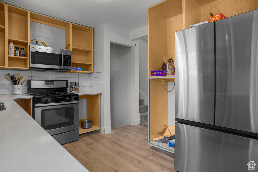 Kitchen with light wood finished floors, open shelves, stainless steel appliances, light countertops, and tasteful backsplash