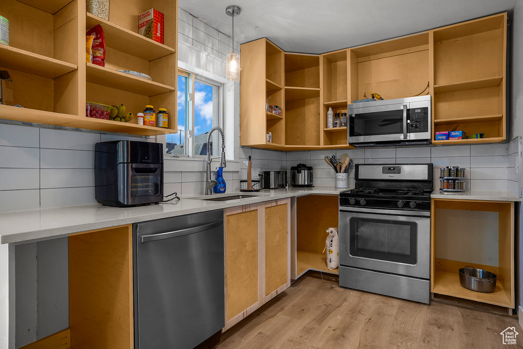 Kitchen featuring open shelves, a sink, light countertops, light wood-style floors, and appliances with stainless steel finishes