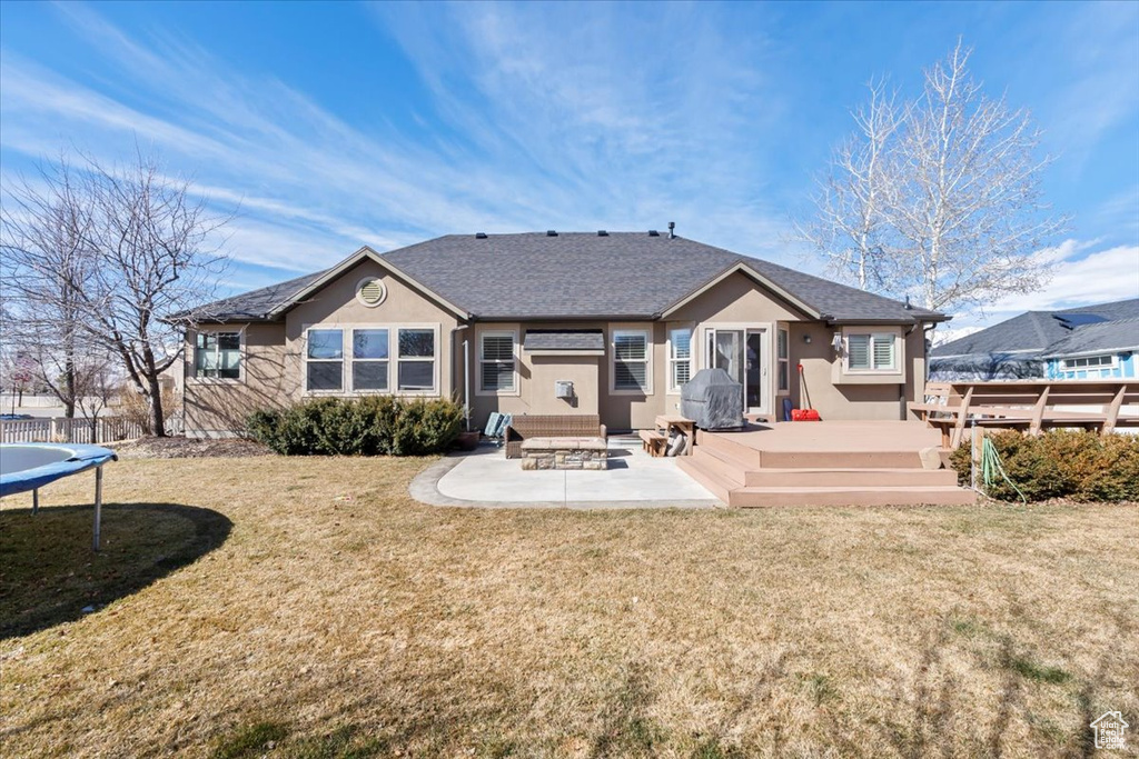 Back of property with a patio, a trampoline, a lawn, and stucco siding