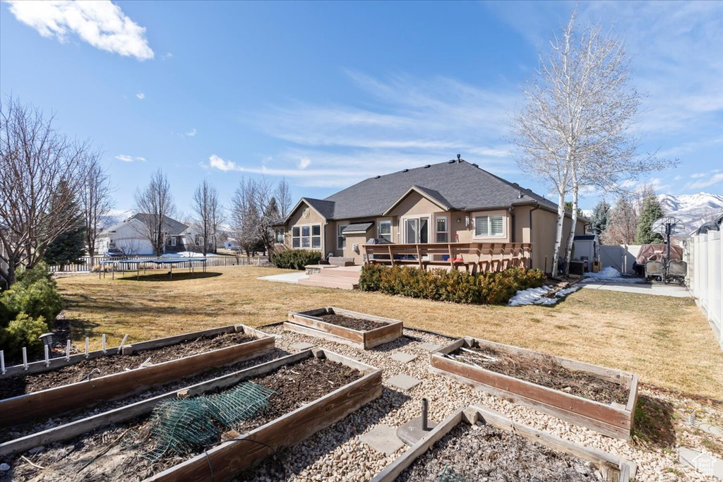 Back of house with a trampoline, a wooden deck, a lawn, a fenced backyard, and a vegetable garden