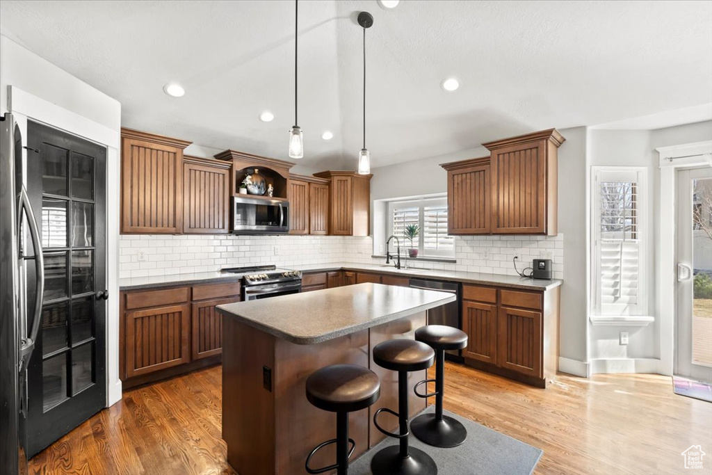 Kitchen featuring a breakfast bar, decorative backsplash, wood finished floors, and stainless steel appliances