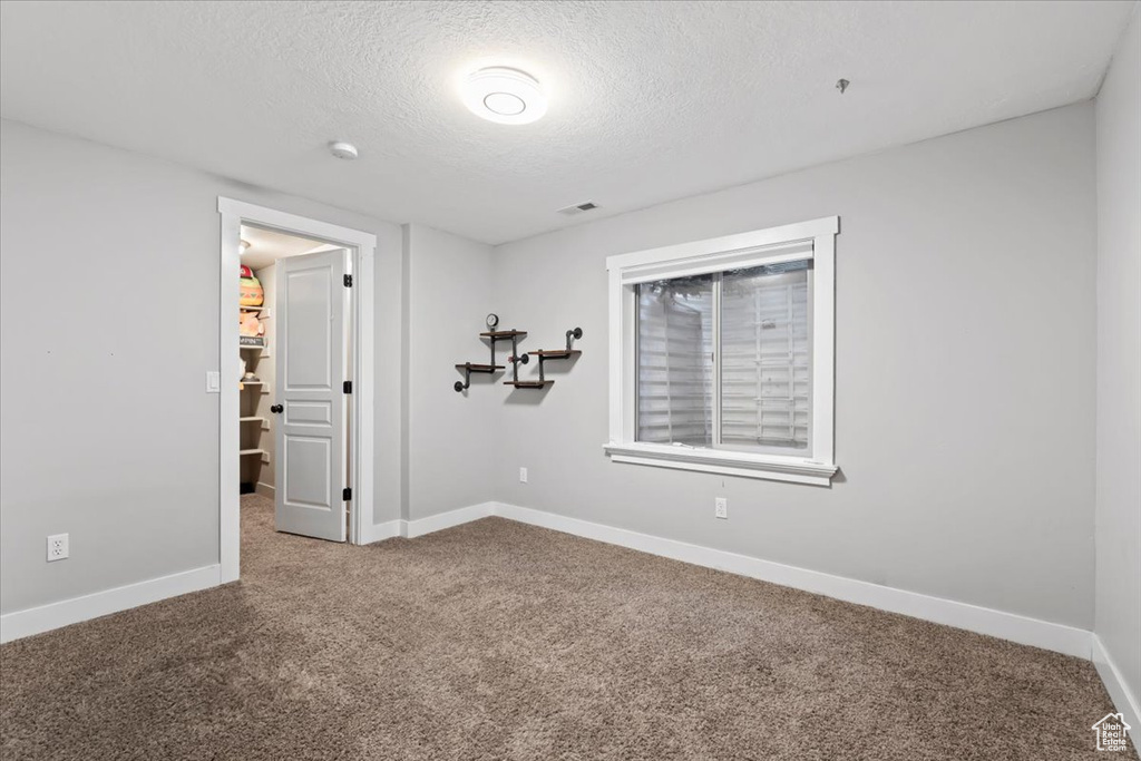 Empty room with a textured ceiling, carpet, visible vents, and baseboards