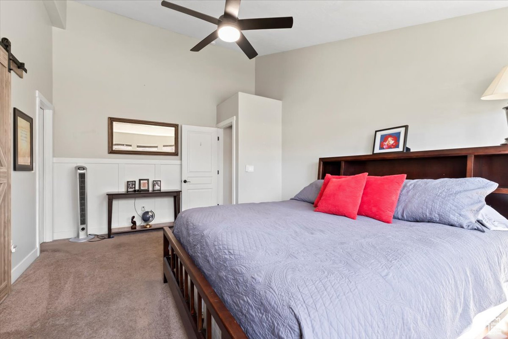 Carpeted bedroom featuring a ceiling fan, a high ceiling, and a barn door