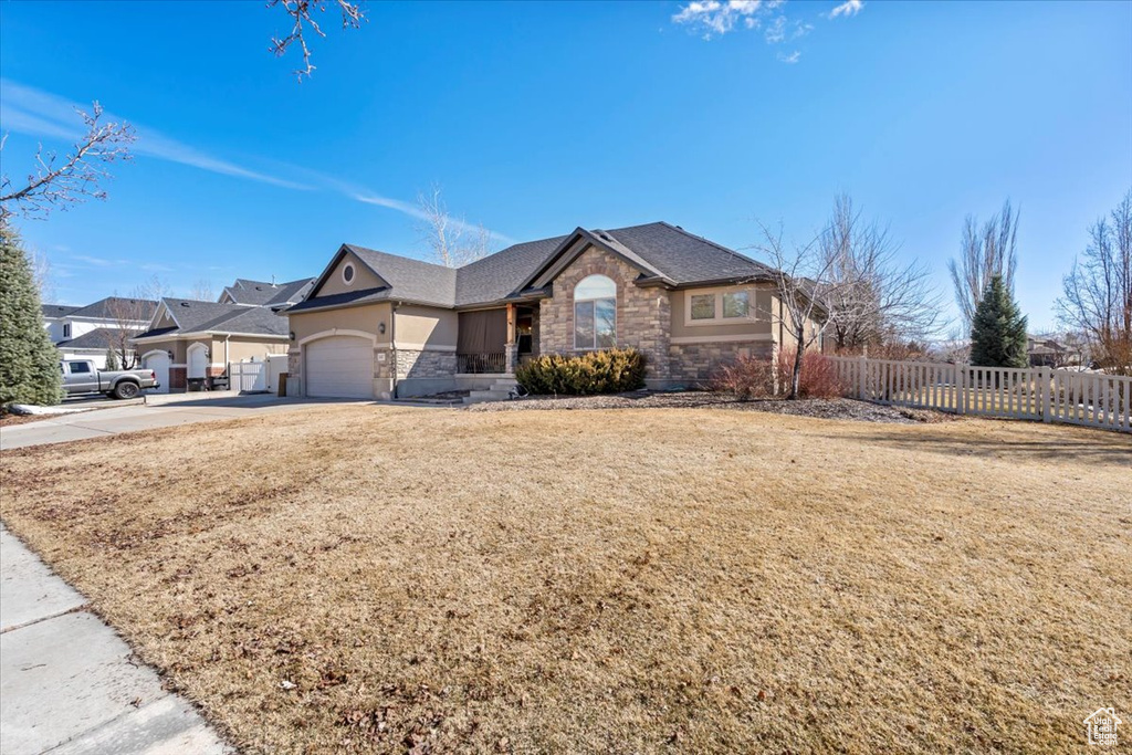 View of front of house with a front lawn, stone siding, fence, concrete driveway, and a garage