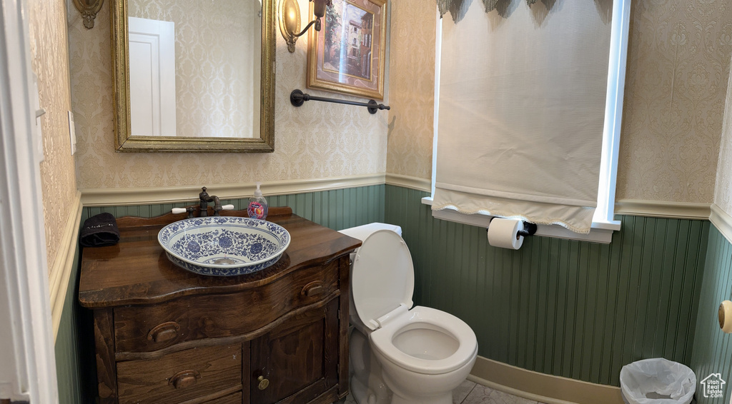 Half bathroom with a sink, toilet, wainscoting, and wallpapered walls