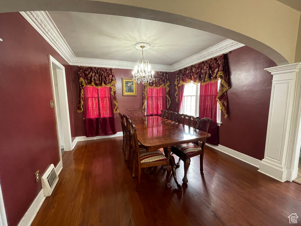 Dining room featuring ornamental molding, wood finished floors, arched walkways, baseboards, and ornate columns