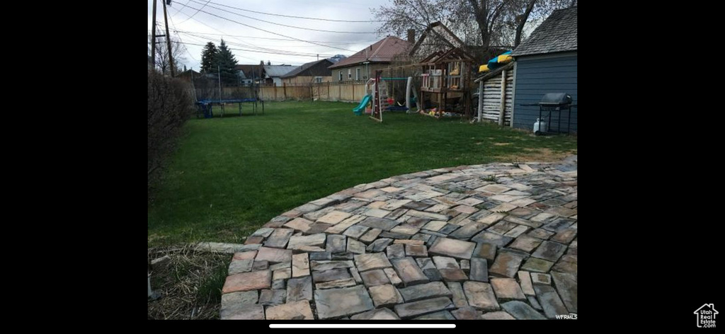 View of yard featuring a patio area, a playground, a trampoline, and fence