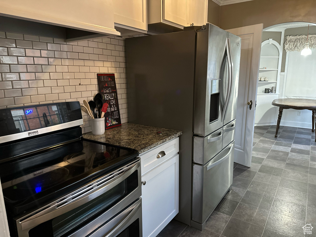 Kitchen featuring dark stone counters, tasteful backsplash, appliances with stainless steel finishes, and white cabinets
