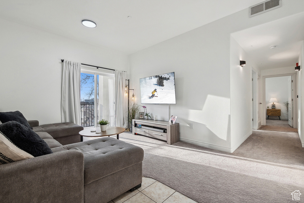 Living area featuring light tile patterned floors, baseboards, visible vents, and light carpet