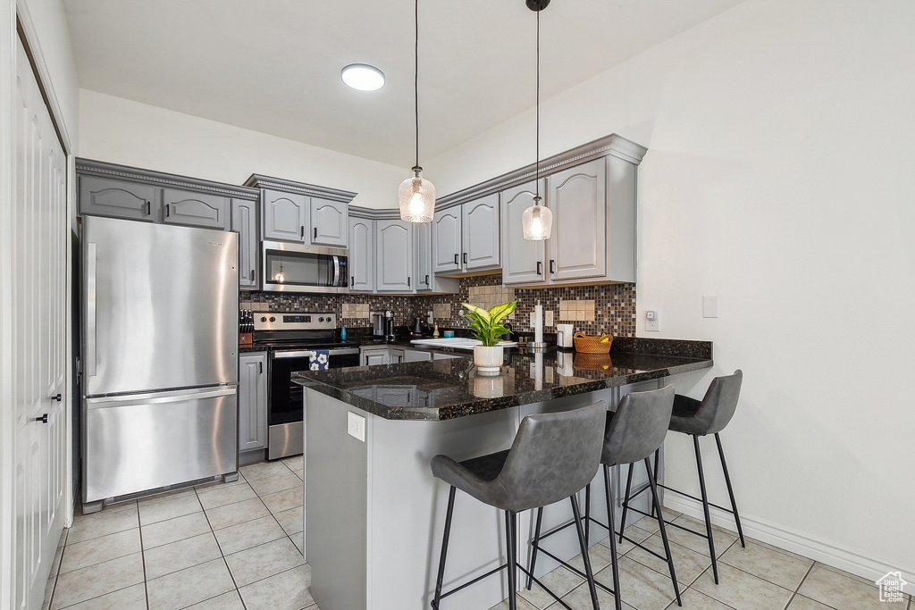 Kitchen with a peninsula, light tile patterned flooring, gray cabinets, stainless steel appliances, and backsplash