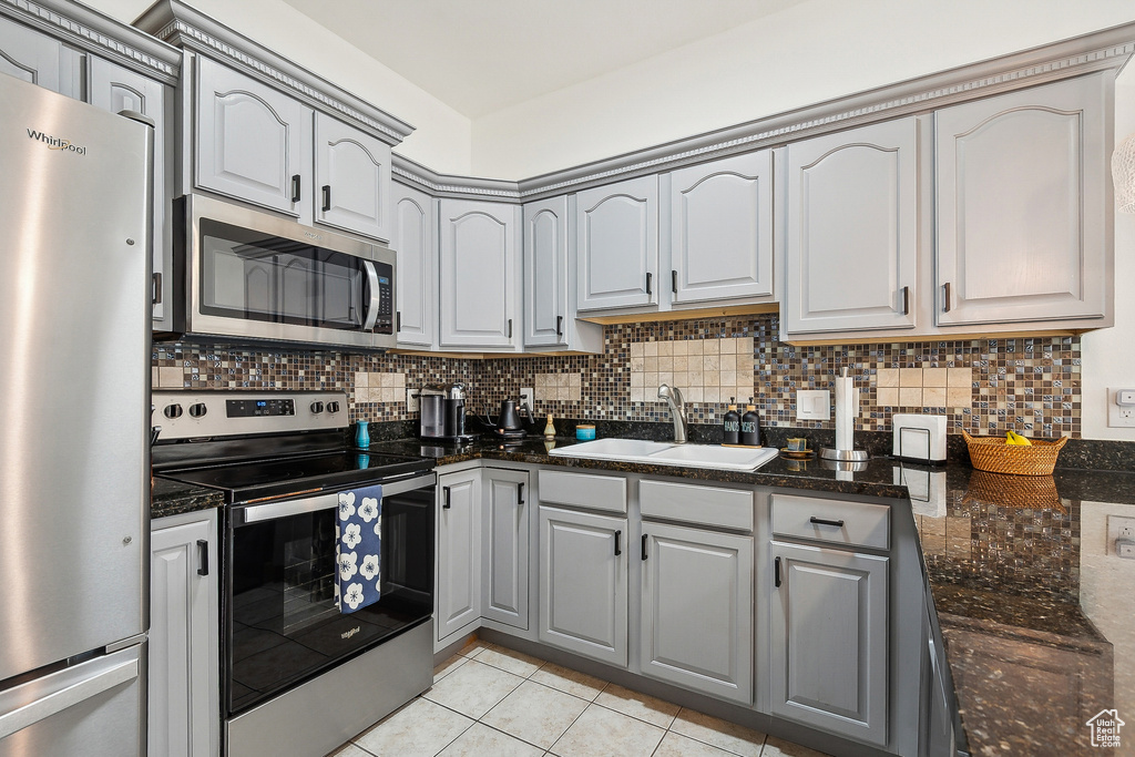 Kitchen with tasteful backsplash, light tile patterned floors, gray cabinets, appliances with stainless steel finishes, and a sink