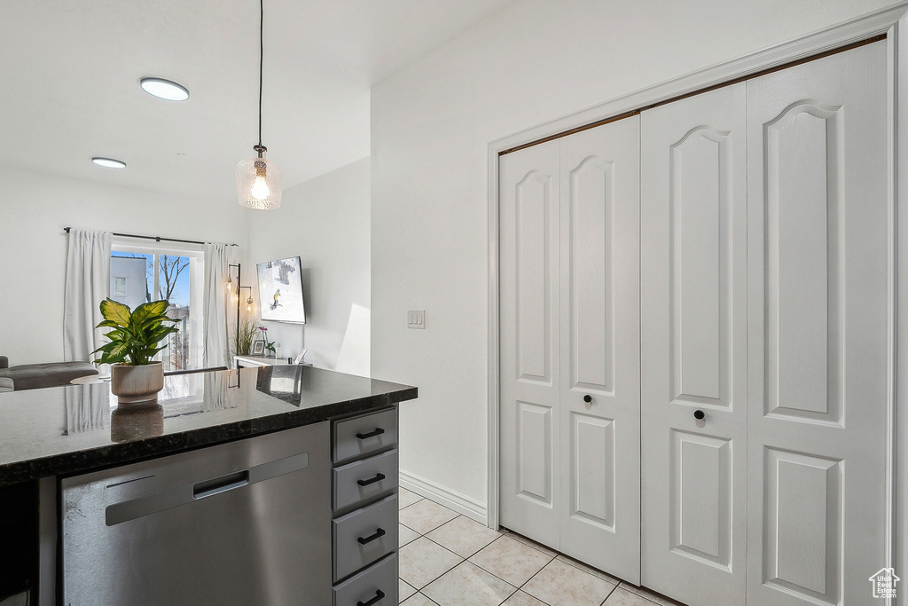 Kitchen with dishwasher, dark stone counters, decorative light fixtures, and light tile patterned floors