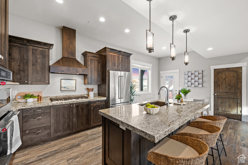 Kitchen featuring premium range hood, dark wood-style flooring, a kitchen breakfast bar, stainless steel appliances, and a sink
