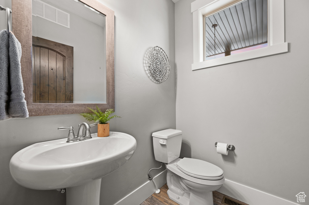 Bathroom featuring wood finished floors, baseboards, visible vents, a sink, and toilet