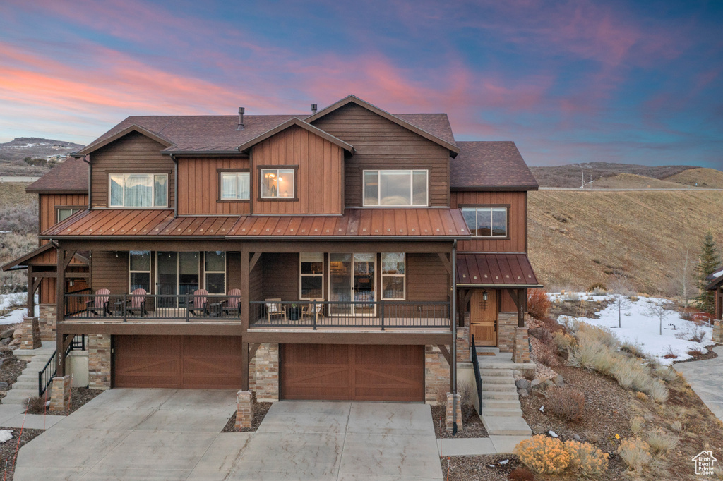 Rustic home featuring a standing seam roof, a garage, stone siding, and driveway
