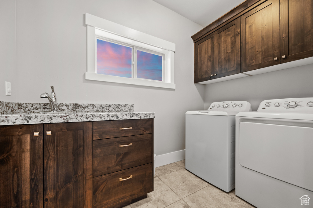 Clothes washing area featuring baseboards, washing machine and clothes dryer, light tile patterned flooring, cabinet space, and a sink