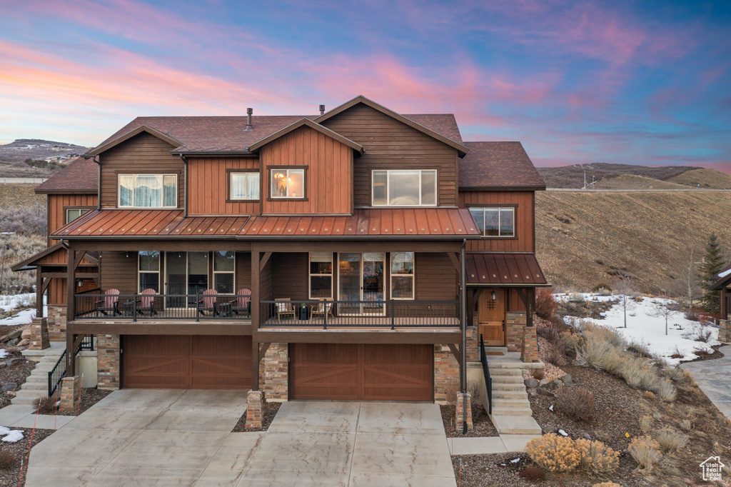 Rustic home featuring stone siding, a garage, driveway, and a standing seam roof