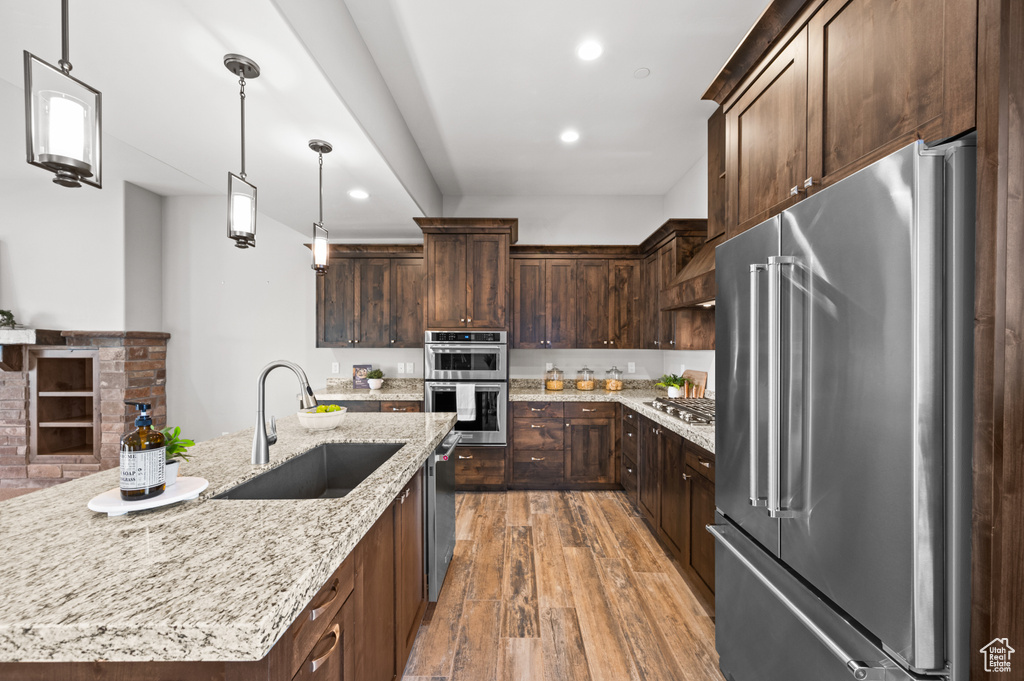 Kitchen with light wood-style flooring, a sink, hanging light fixtures, dark brown cabinetry, and stainless steel appliances