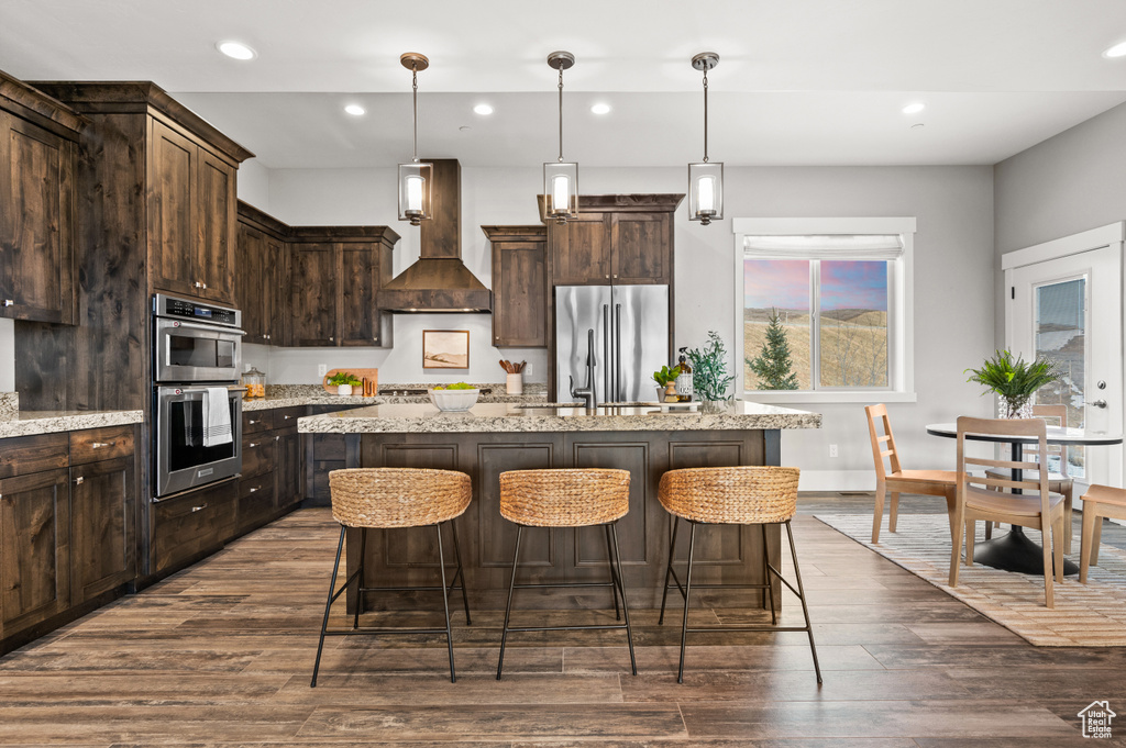 Kitchen featuring stainless steel appliances, dark brown cabinets, an island with sink, and custom range hood
