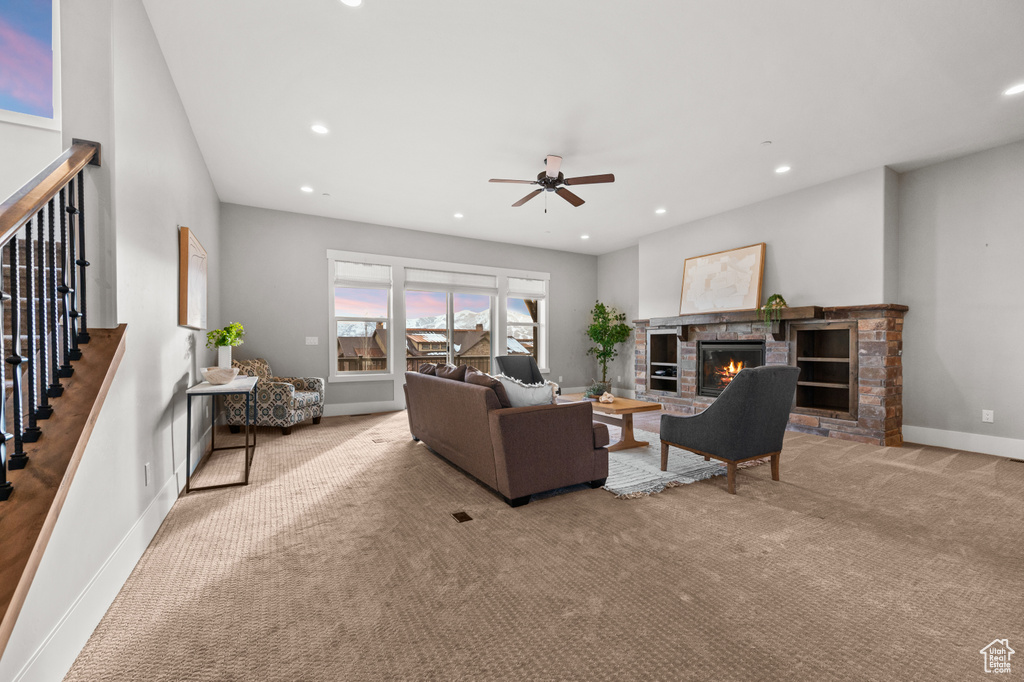 Carpeted living area with a stone fireplace, recessed lighting, stairway, and baseboards