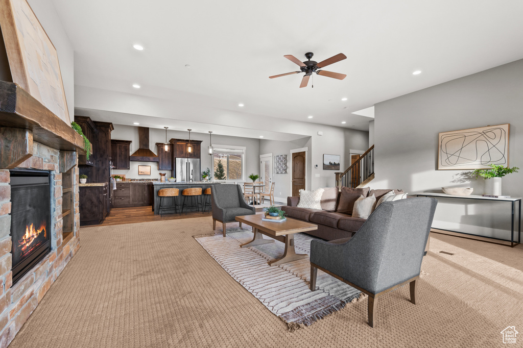 Living area featuring a ceiling fan, recessed lighting, a stone fireplace, light colored carpet, and stairs