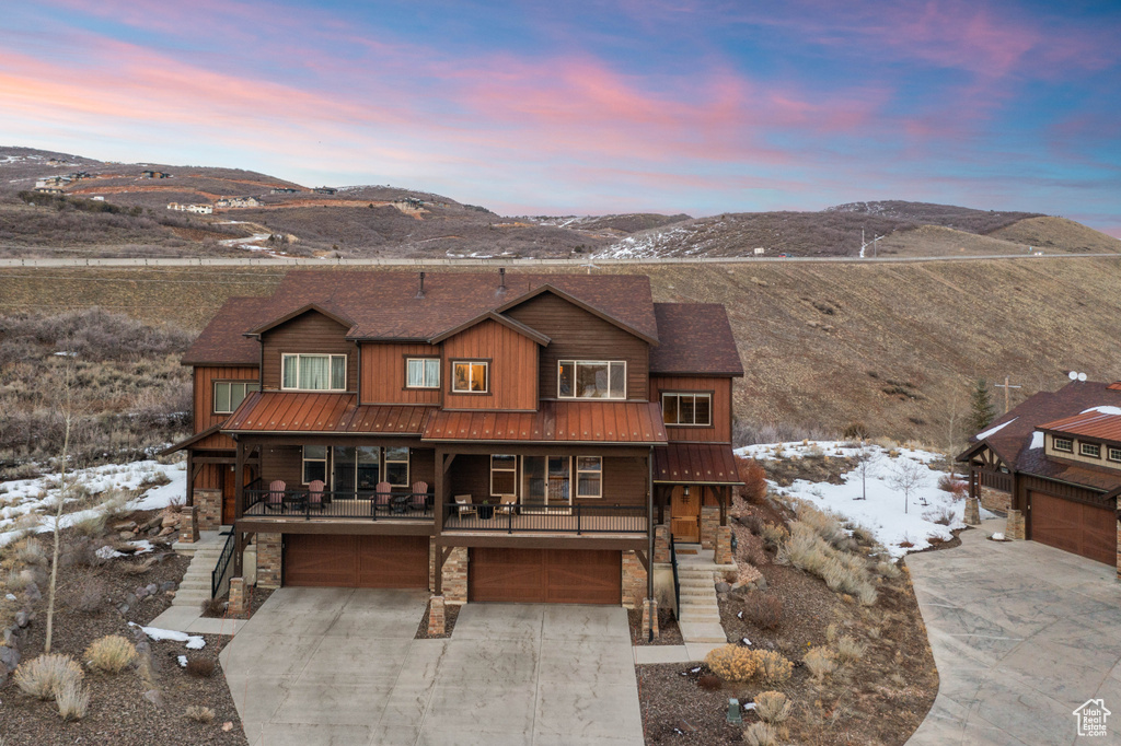 Rustic home with an attached garage, concrete driveway, stairs, stone siding, and a mountain view
