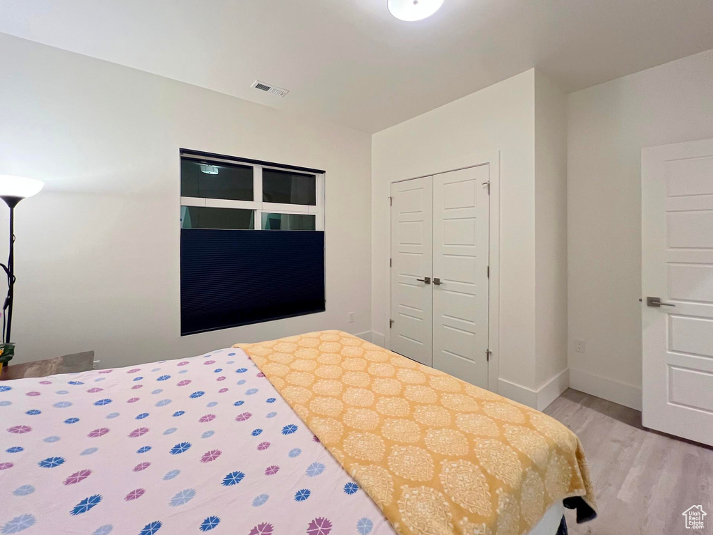 Bedroom featuring light wood finished floors, baseboards, visible vents, and a closet