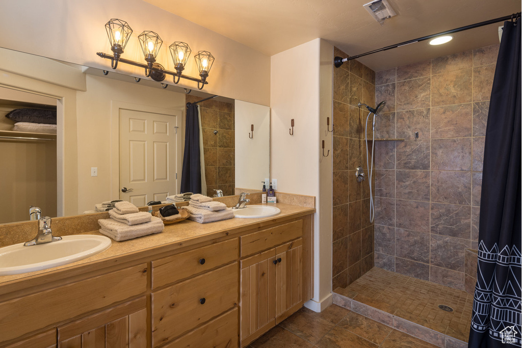 Full bath with a sink, visible vents, tiled shower, and double vanity