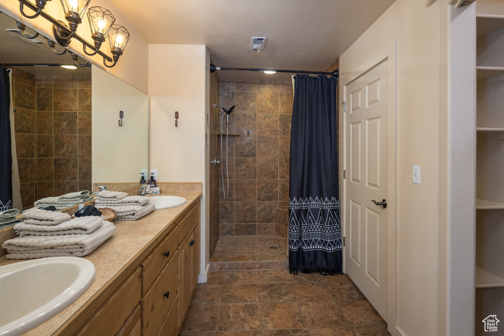 Bathroom with a sink, a notable chandelier, double vanity, and a tile shower