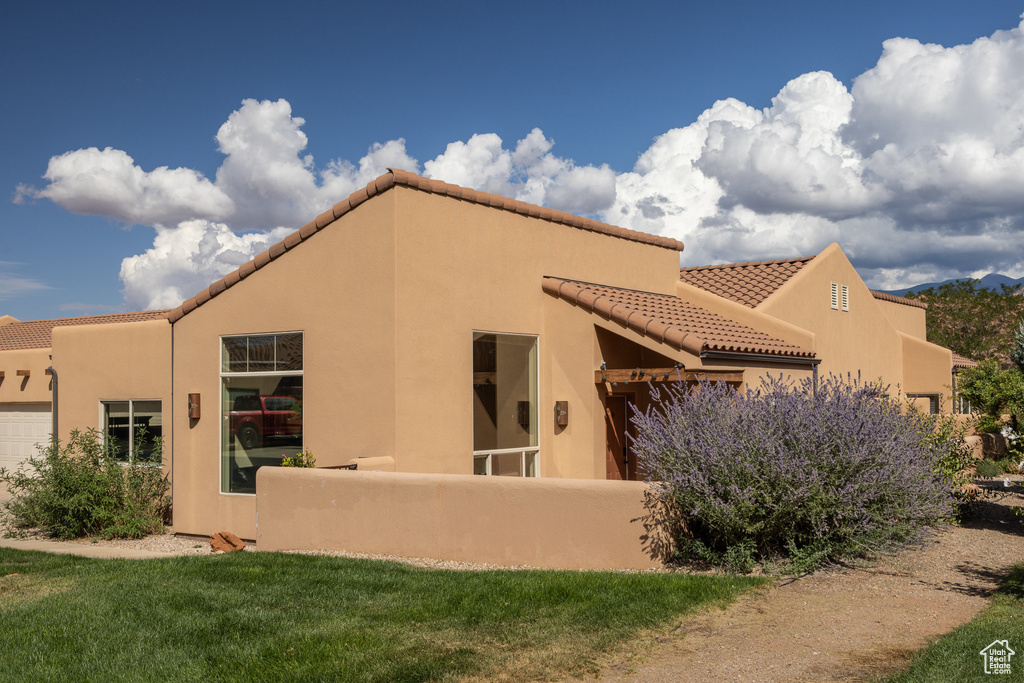 Back of house with stucco siding, an attached garage, and a tiled roof