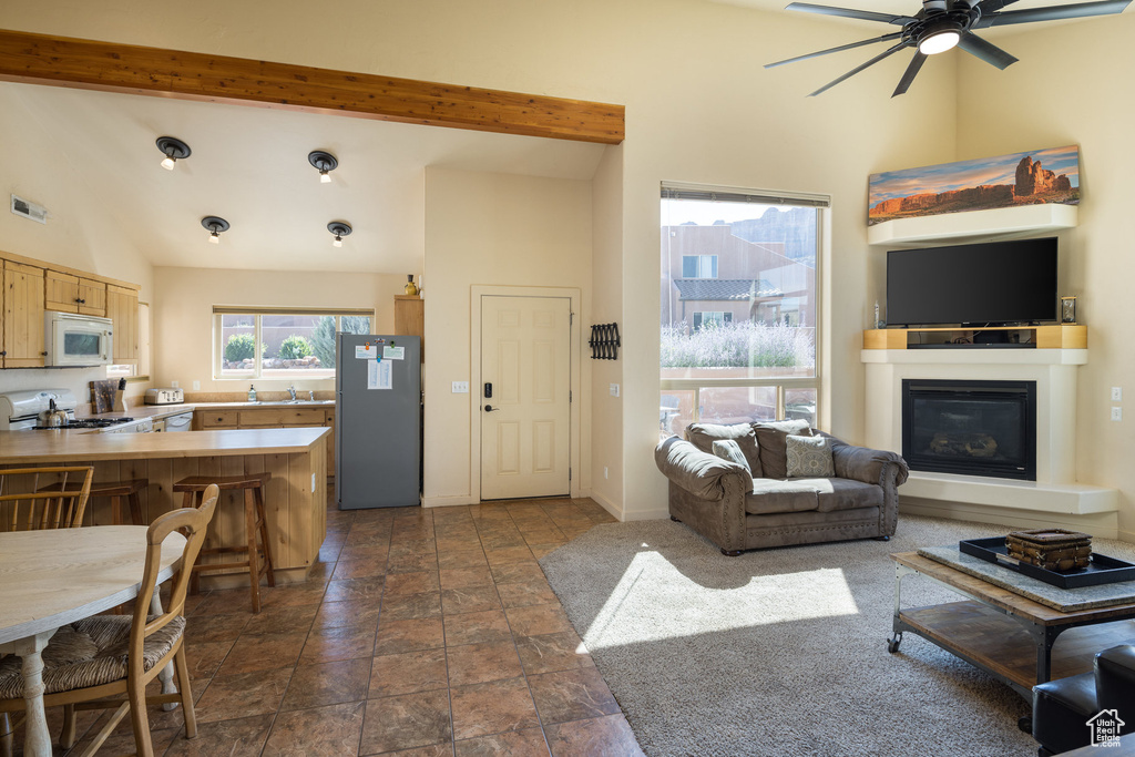 Living room with beamed ceiling, visible vents, high vaulted ceiling, a ceiling fan, and a glass covered fireplace