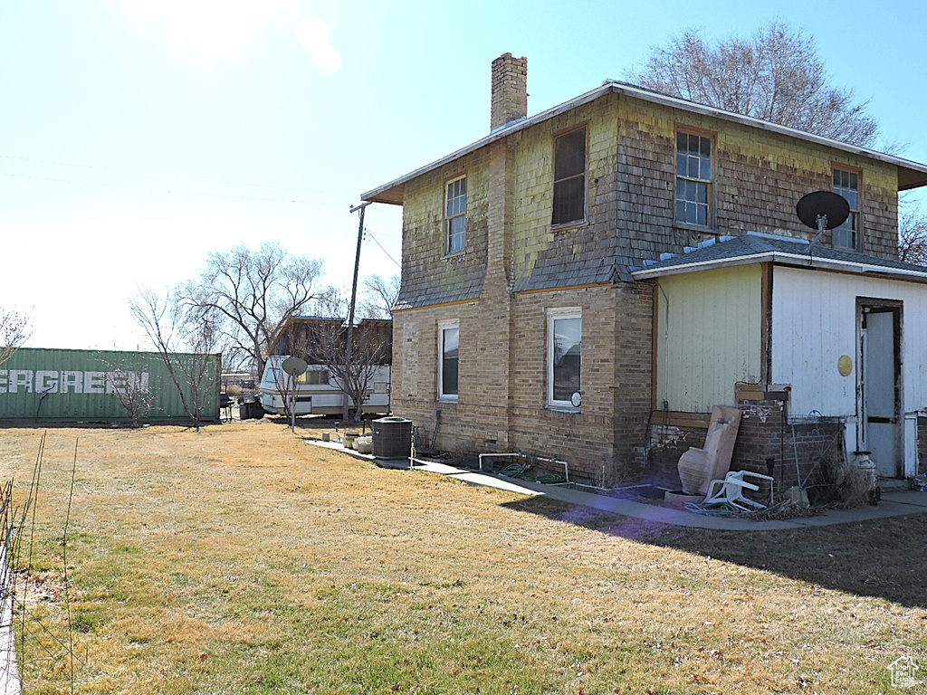 Rear view of house with central air condition unit, a lawn, and a chimney