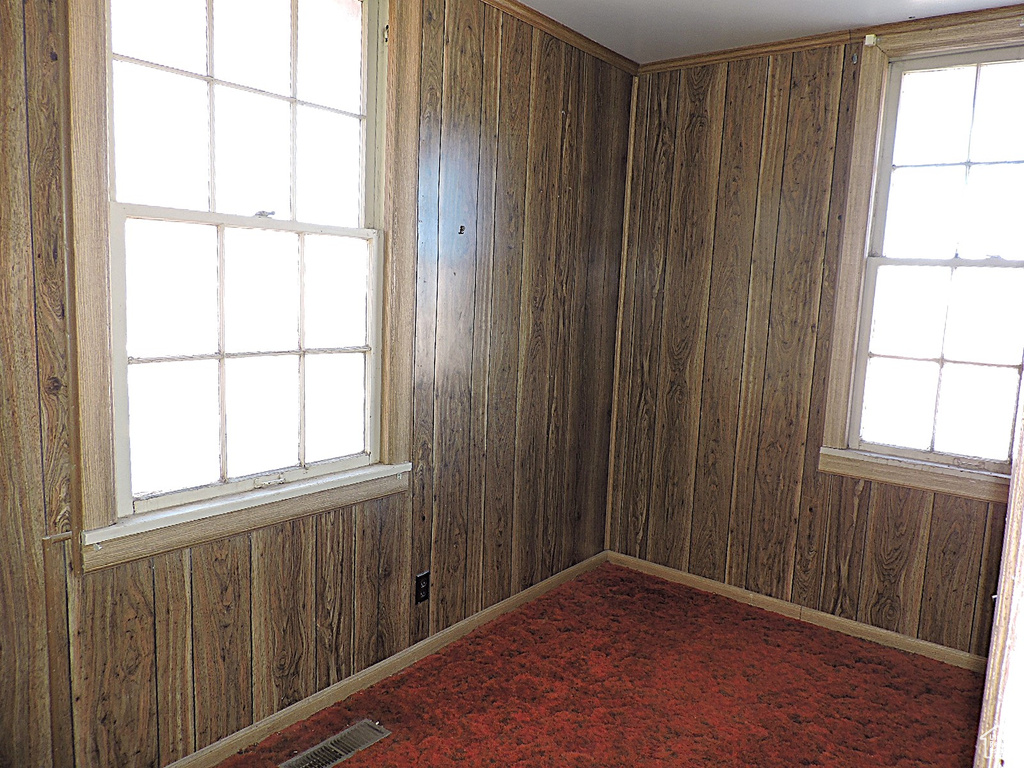 Unfurnished room featuring visible vents, baseboards, carpet, and wooden walls