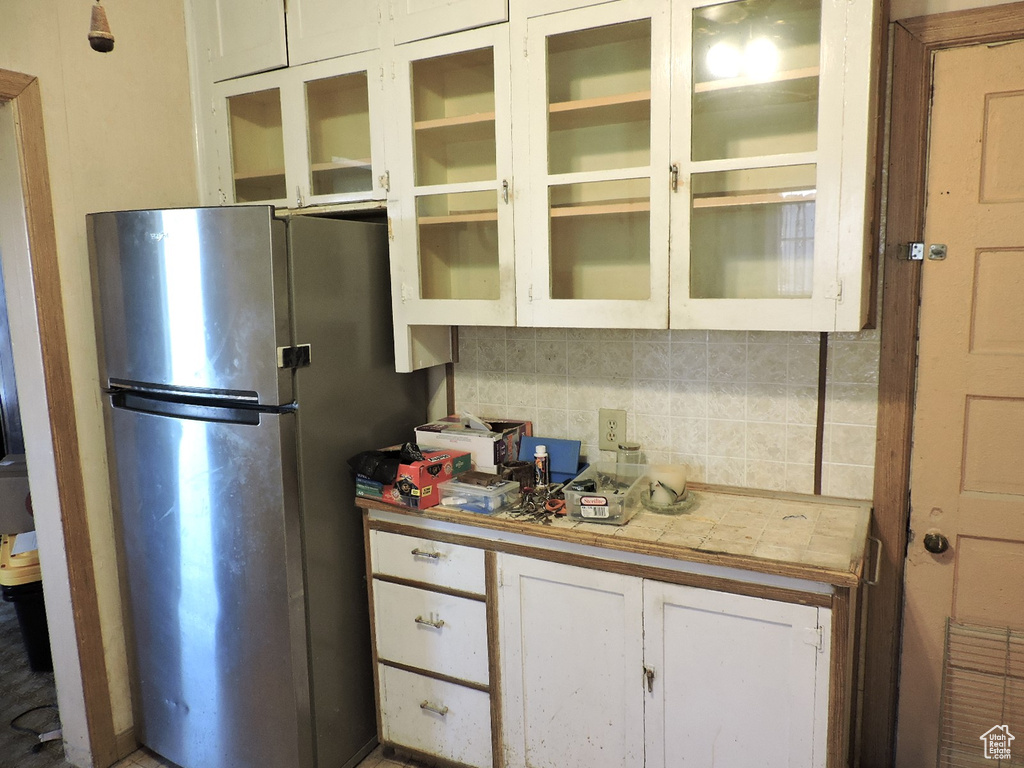 Kitchen with glass insert cabinets, tasteful backsplash, white cabinets, and freestanding refrigerator