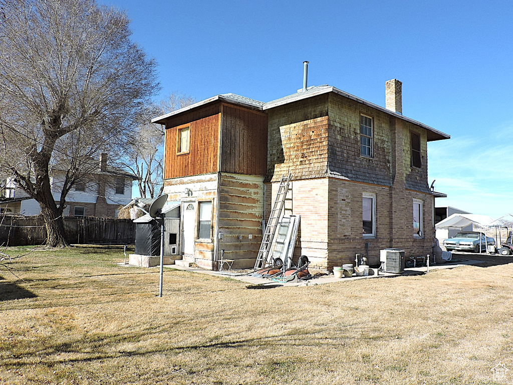 Rear view of property with central air condition unit, a lawn, fence, and a chimney