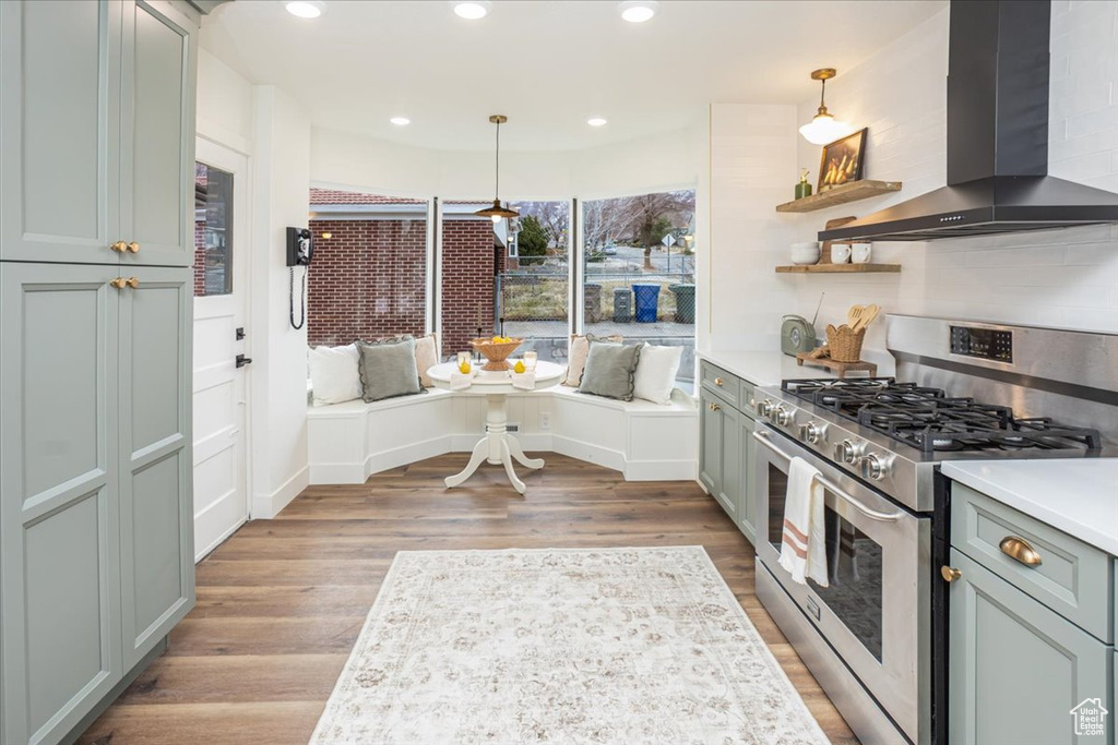 Kitchen with stainless steel range with gas cooktop, wood finished floors, light countertops, and wall chimney range hood