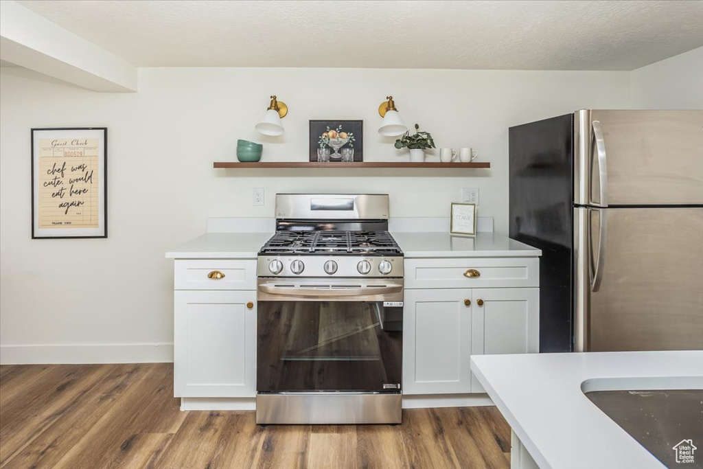 Kitchen featuring open shelves, wood finished floors, light countertops, and appliances with stainless steel finishes