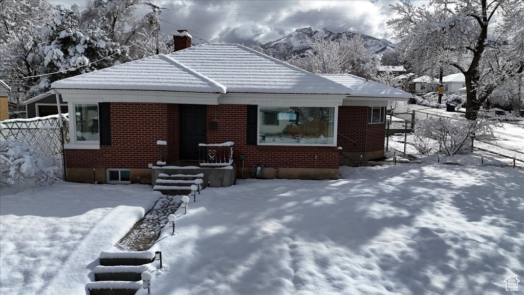 Snow covered back of property with a tile roof, fence, a mountain view, brick siding, and a chimney