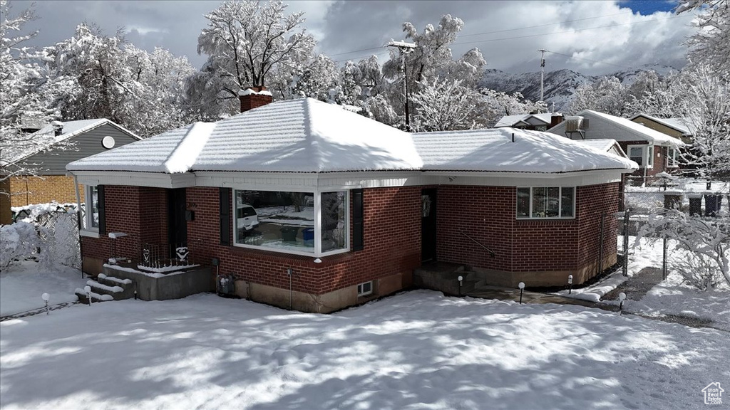 View of snow covered exterior featuring brick siding, a tile roof, and a chimney