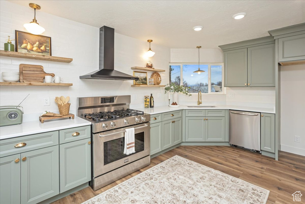 Kitchen featuring green cabinetry, open shelves, a sink, appliances with stainless steel finishes, and wall chimney range hood