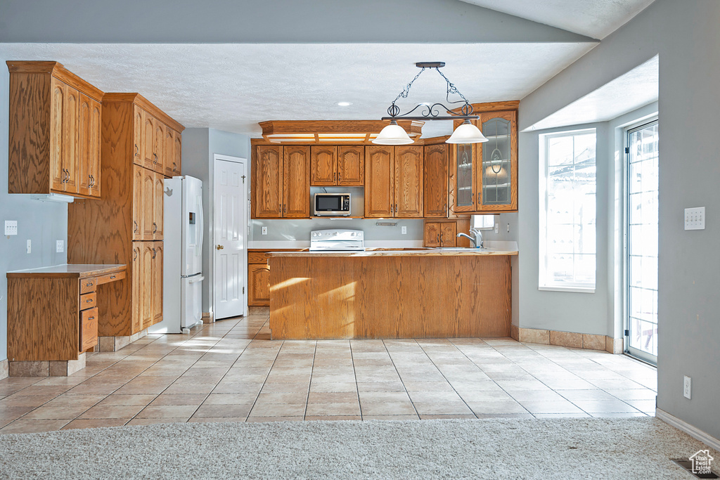 Kitchen with stainless steel microwave, brown cabinets, a peninsula, white refrigerator with ice dispenser, and range