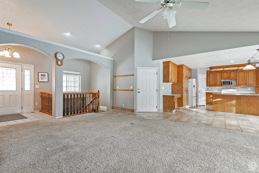 Unfurnished living room featuring light carpet, high vaulted ceiling, ceiling fan with notable chandelier, light tile patterned floors, and baseboards