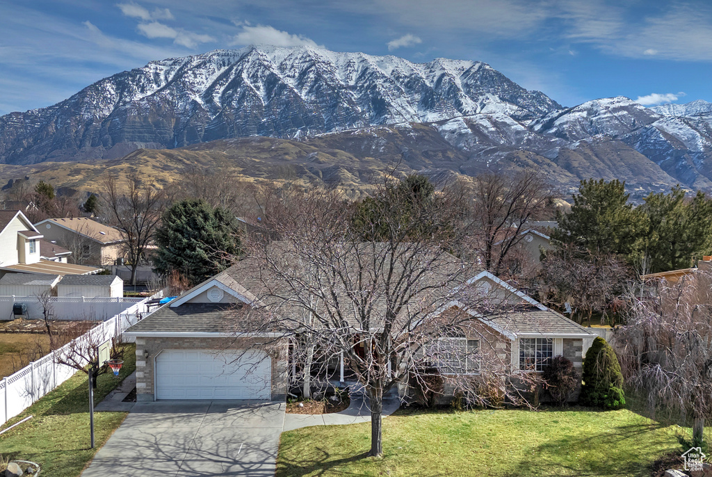 View of front of house with a mountain view, concrete driveway, a front yard, and fence