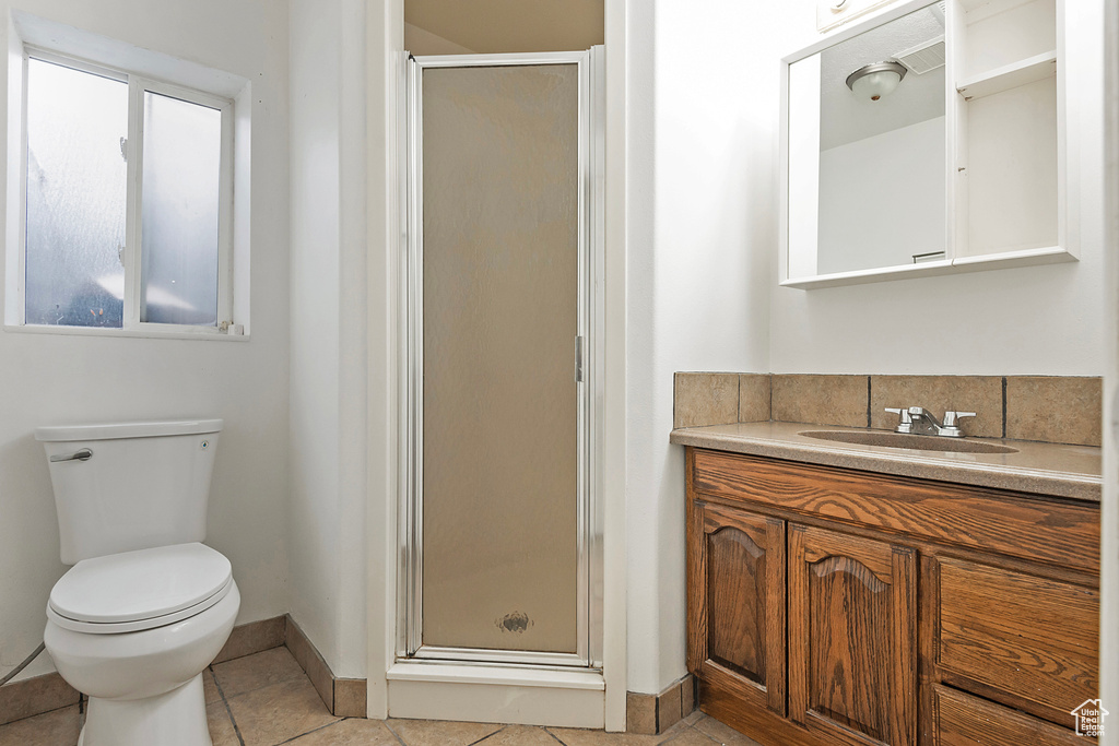 Bathroom featuring vanity, baseboards, a stall shower, tile patterned flooring, and toilet