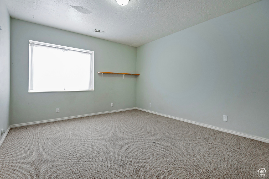 Carpeted spare room with baseboards, visible vents, and a textured ceiling