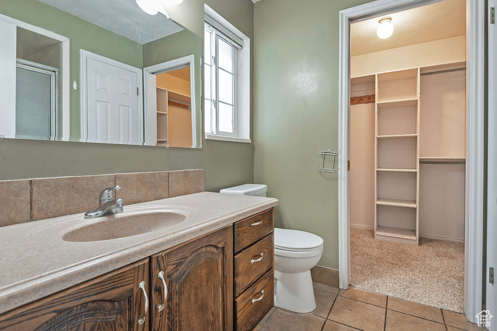 Full bathroom featuring vanity, tile patterned flooring, a shower stall, a walk in closet, and toilet