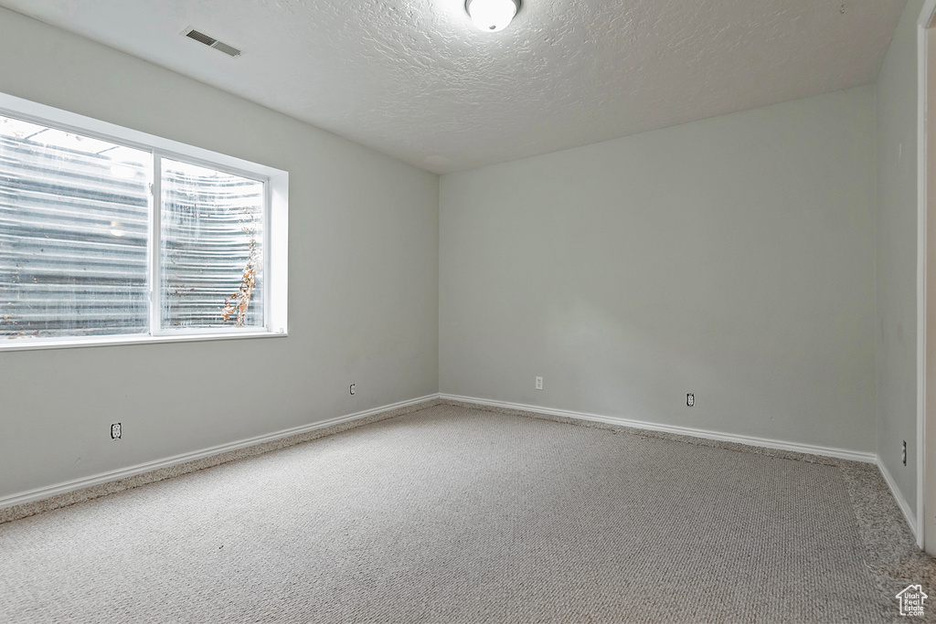 Empty room featuring baseboards, carpet, visible vents, and a textured ceiling