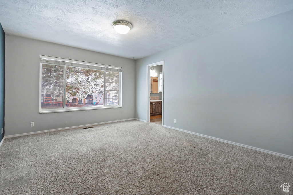 Carpeted empty room featuring visible vents, baseboards, and a textured ceiling