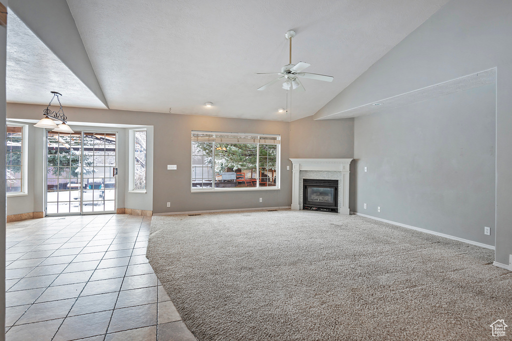 Unfurnished living room with light carpet, a ceiling fan, a glass covered fireplace, light tile patterned floors, and baseboards